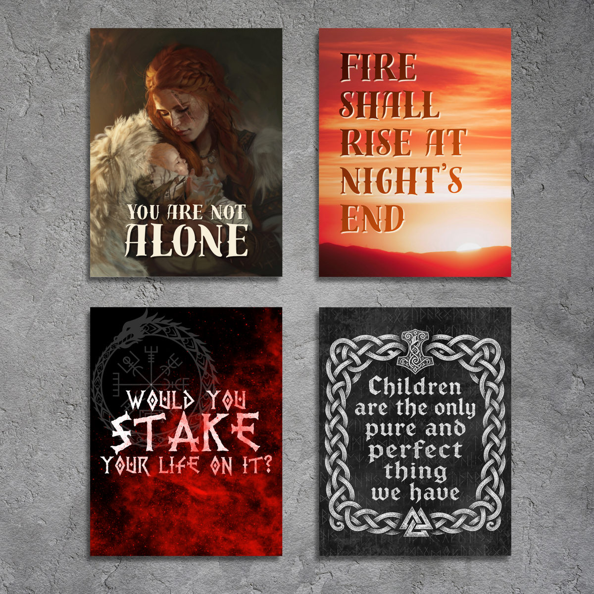Four square wall art prints arranged in a 2x2 grid on a textured gray wall. The prints feature Norse-themed designs: a dark fantasy illustration of a woman with the text 'YOU ARE NOT ALONE', a fiery sunset scene with the text 'FIRE SHALL RISE AT NIGHT'S END', a red and black graphic with the text 'WOULD YOU STAKE YOUR LIFE ON IT?', and a black print with a silver Celtic knot border and the text 'Children are the only pure and perfect thing we have'.
