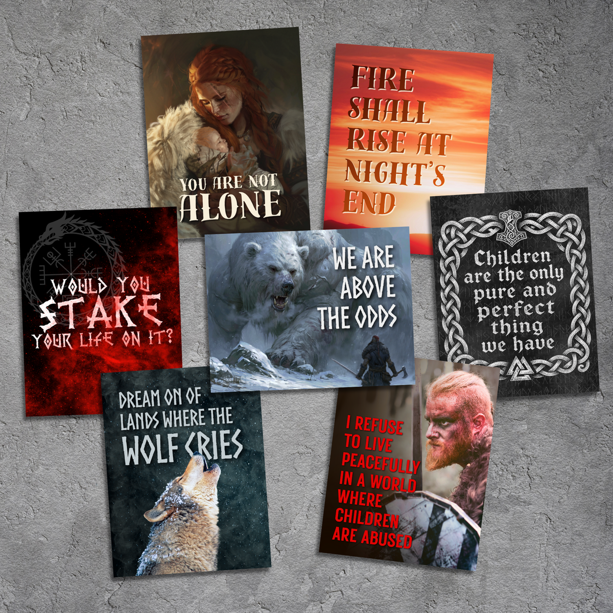 A set of seven themed stickers arranged on a textured gray concrete background. The prints feature various designs with Norse and fantasy themes, including a wolf, a warrior, a bear, and text such as 'YOU ARE NOT ALONE', 'FIRE SHALL RISE AT NIGHT'S END', and 'Children are the only pure and perfect thing we have'.