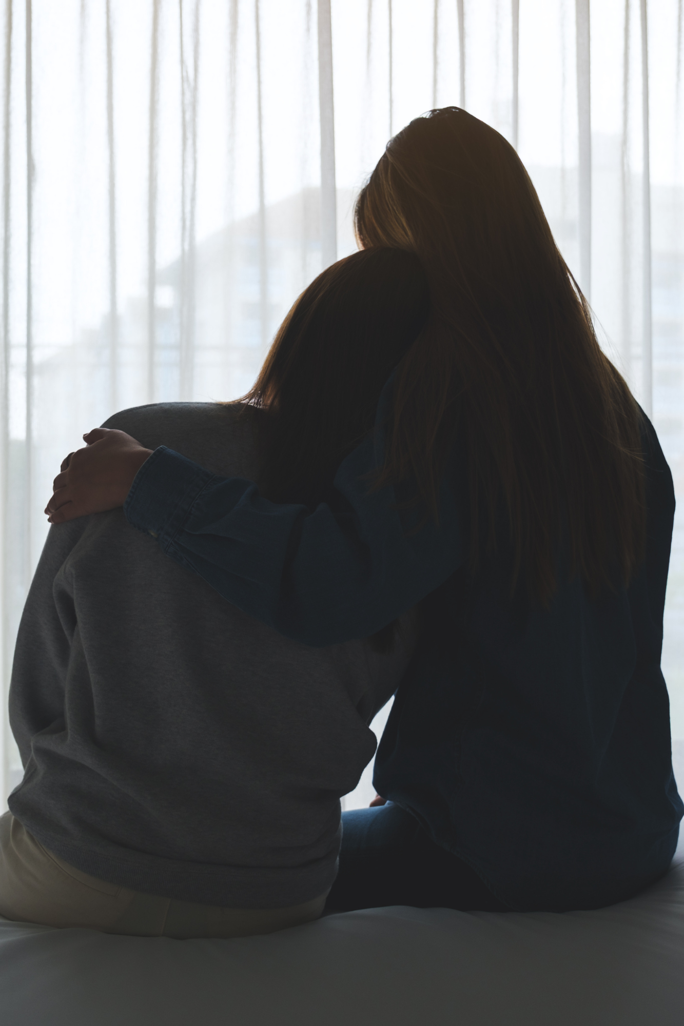 Two people sitting close together in silhouette against a light background